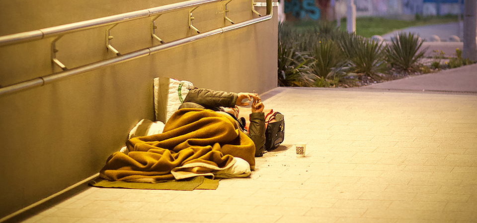 A homeless person lying down in a covered tunnel