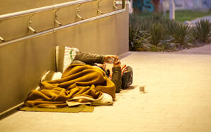 A homeless person lying down in a covered tunnel